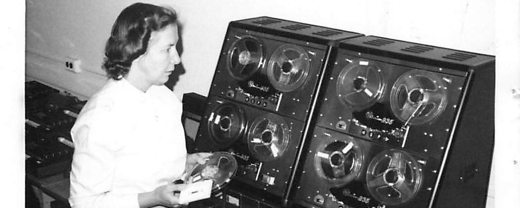 A woman standing near a big audio recording machine