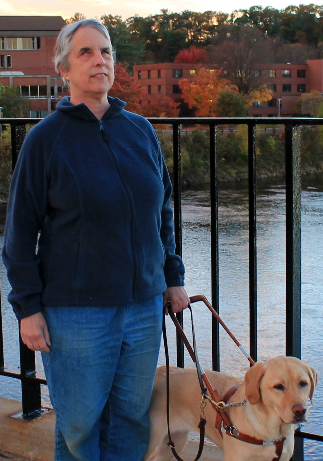 Dr. Kathie pictured with her guide dog on a bridge over a body of water